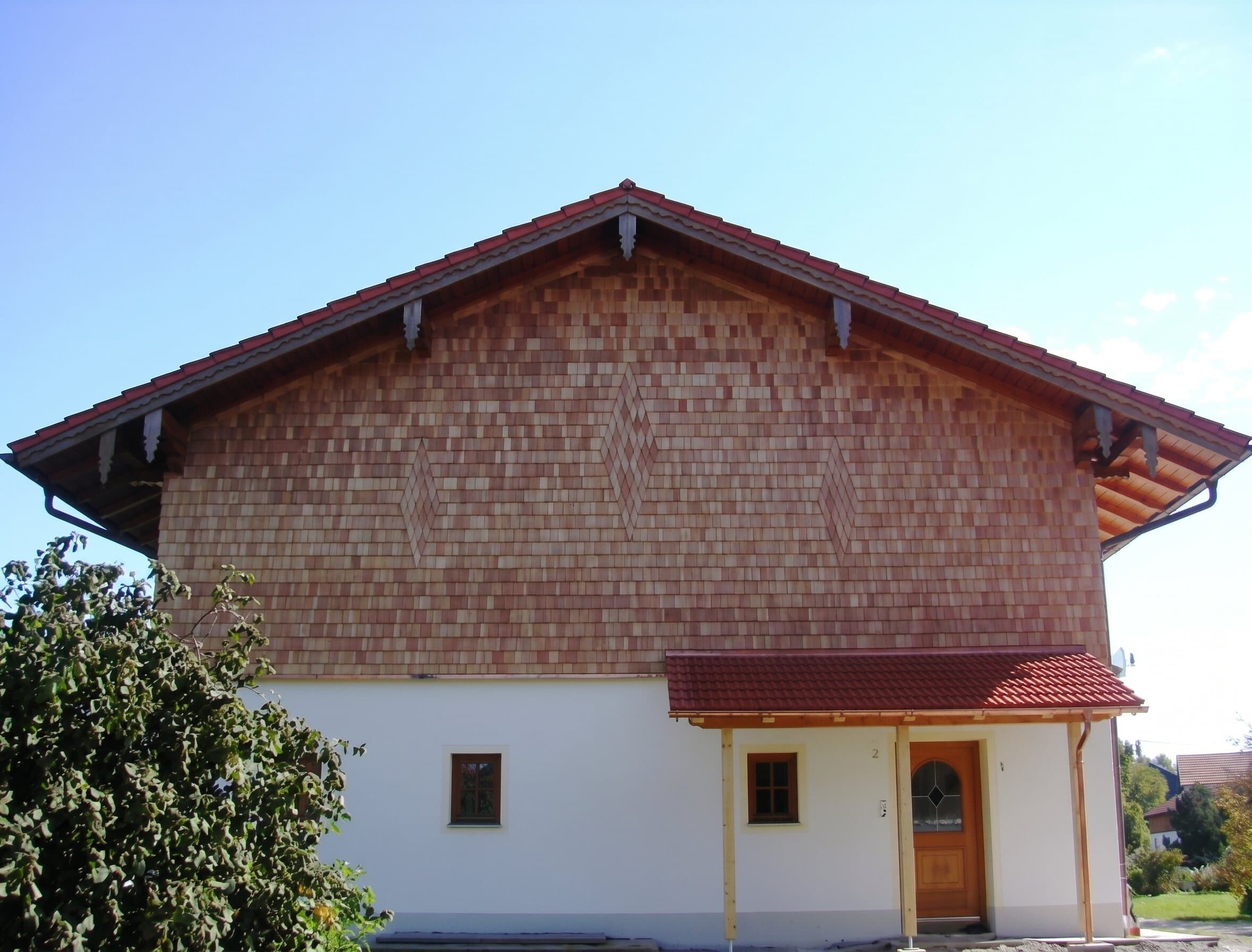 Bauernhaus-Giebel mit Holzschindel-Fassade in warmen Rottönen